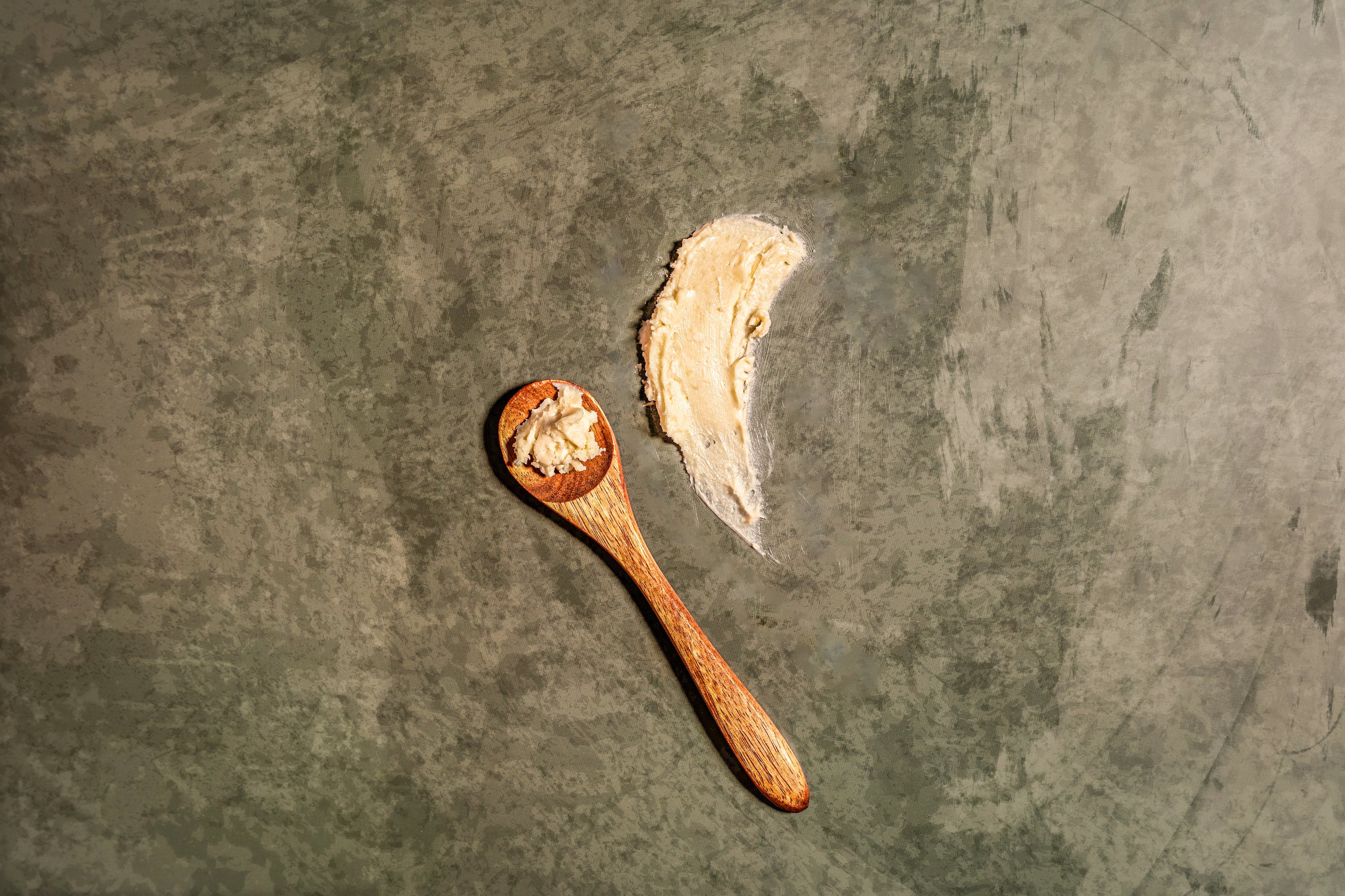 Wooden spoon with a scoop of tea butter on a textured dark surface