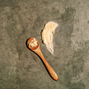 Wooden spoon with a scoop of tea butter on a textured dark surface