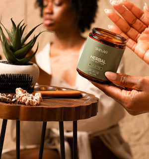 Person holding a jar of Shinar Herbal hair butter with a blurred background
