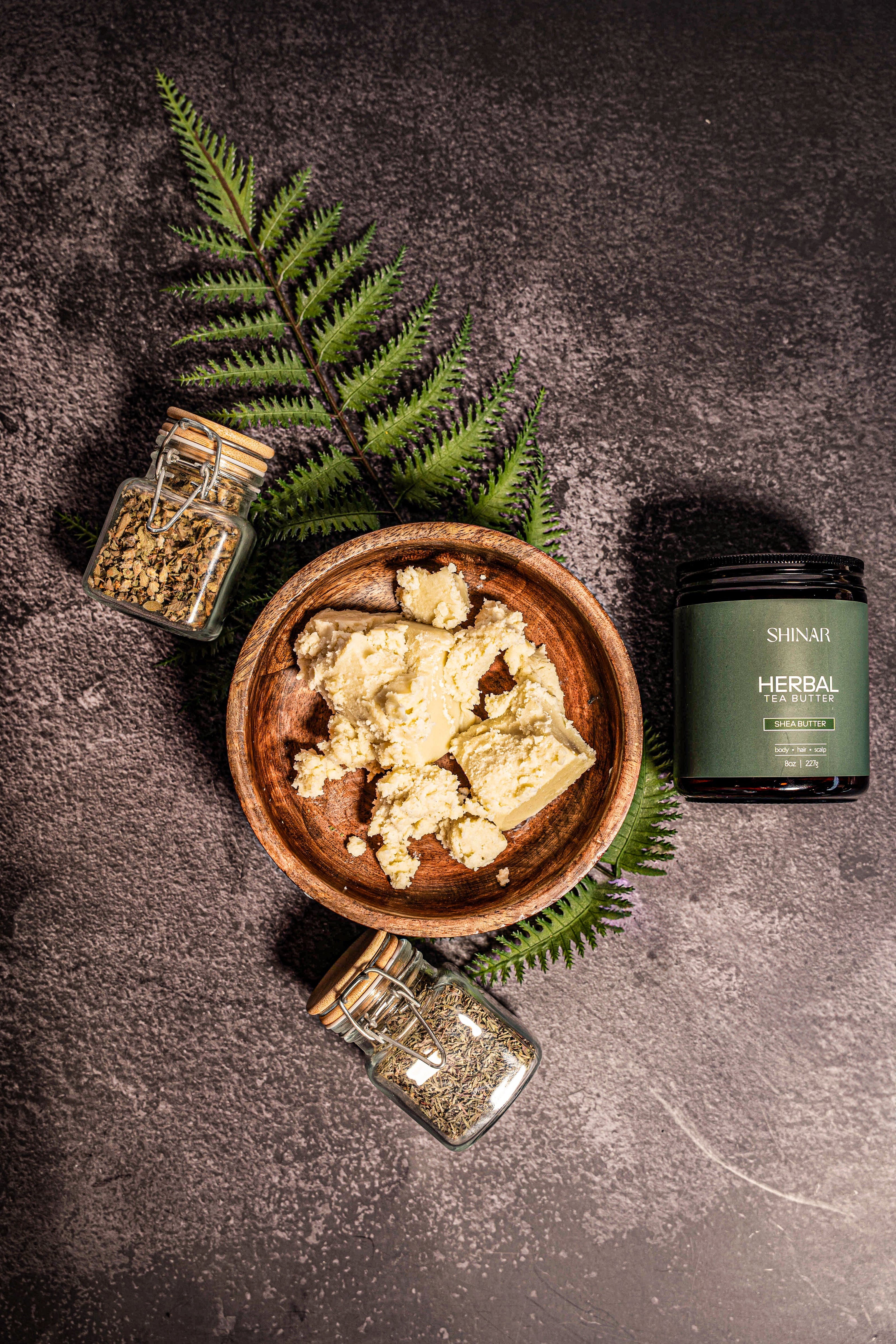 Herbal product in a wooden bowl with jars and fern leaves on a dark surface