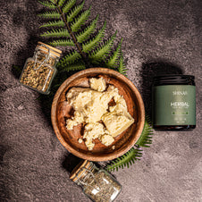 Herbal product in a wooden bowl with jars and fern leaves on a dark surface