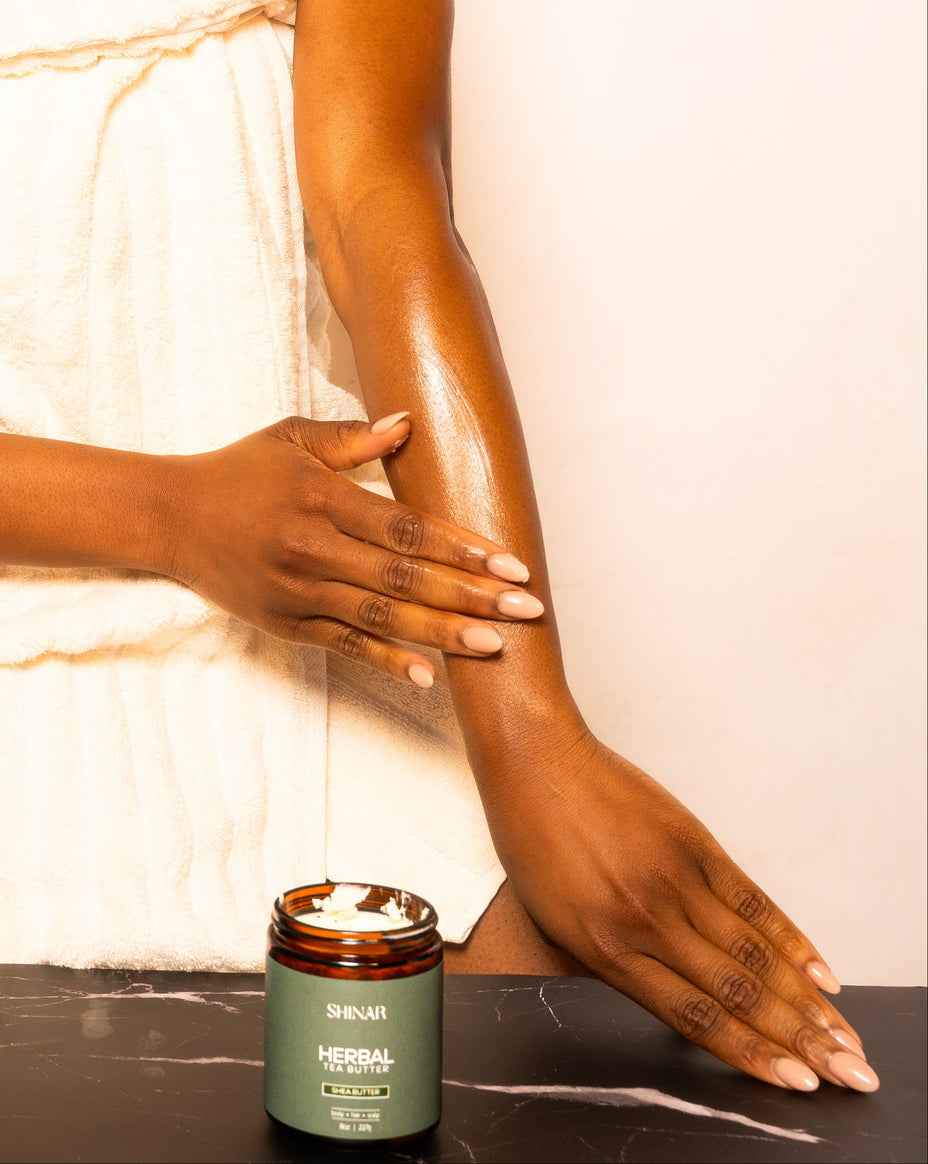 Woman applying cream to her arm with a jar of cream on a table in front of her.