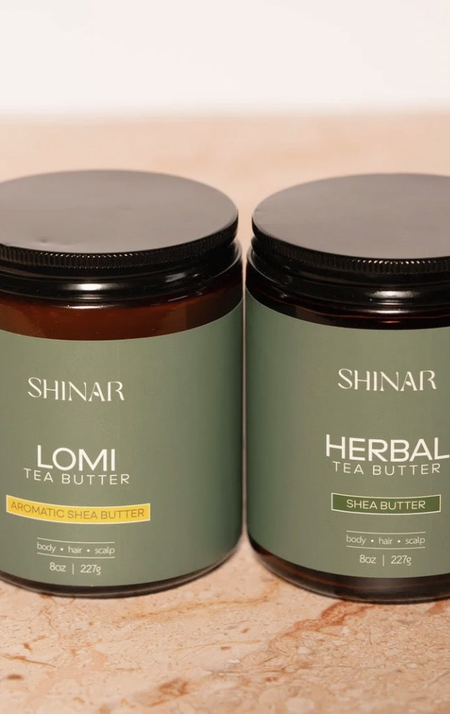 Two jars of Shinar Lomi Tea Butter and Herbal Tea Butter on a beige surface